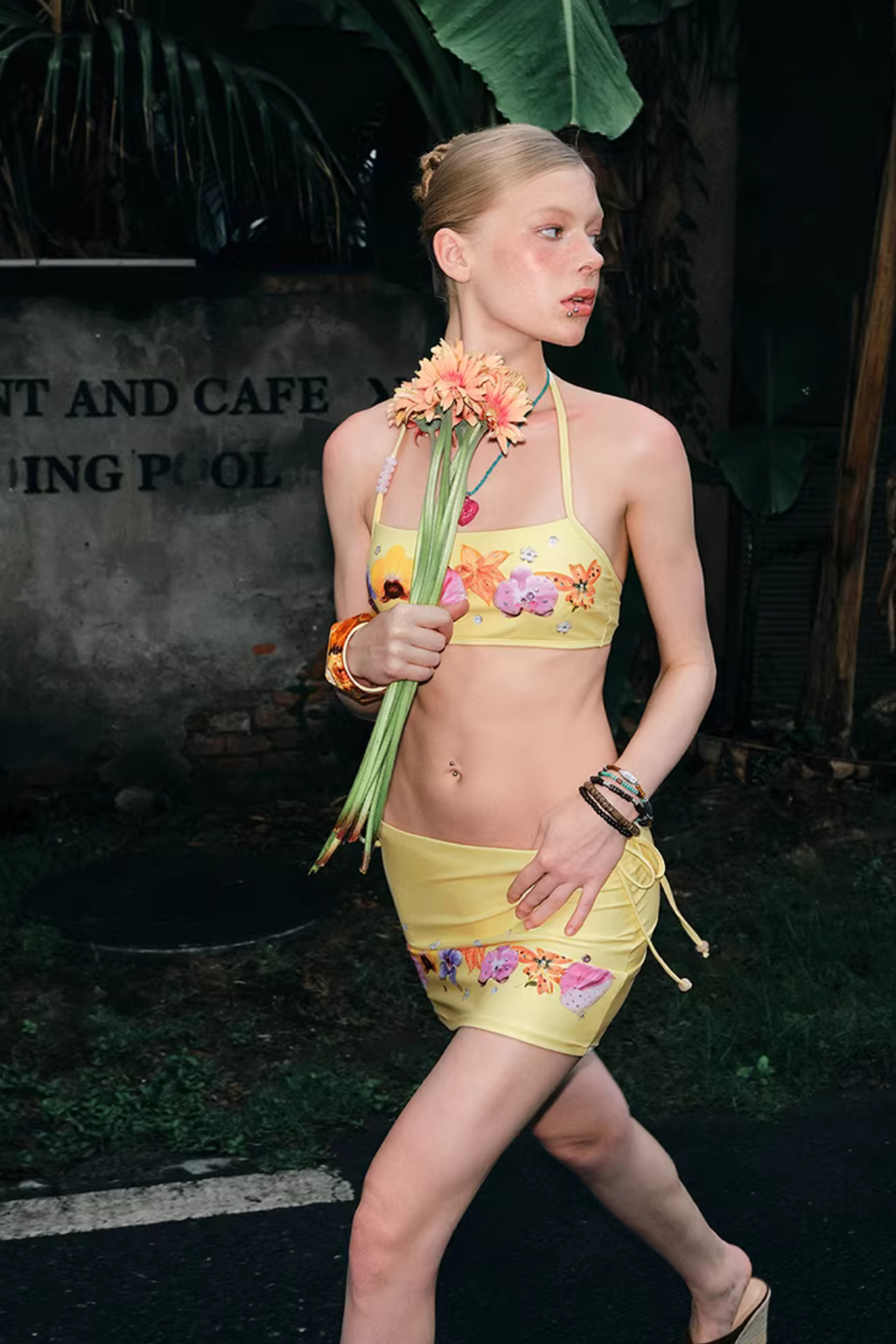 Woman in a yellow bikini with floral designs walking outdoors.
